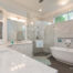 A modern bathroom featuring a marble vanity with dual sinks, a large frameless glass shower, and a freestanding bathtub. The space is bright with natural light from high windows and includes elegant fixtures and decor. A logo reads "William French Home Improvements.