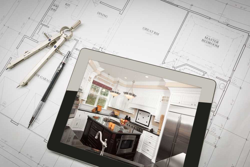 A tablet displaying an image of a modern kitchen with white cabinets, stainless steel appliances, and a black island sits on top of architectural blueprints for a Lewisville home remodel. A compass and a pen are also placed on the blueprints.